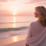 Frau über 50 blickt am Meer in den Sonnenaufgang – Loslassen mit 50plus