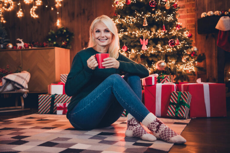 Entspannt durch die Weihnachtszeit mit 50plus - blonde Frau über 50 sitzt mit einer Tasse Tee entspannt vor dem Weihnachtsbaum