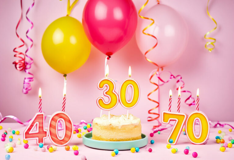 Runde Geburtstage mit 50plus - Geburtstagstorte, runde Zahlen, Luftballons, Kerzen und Luftschlangen vor rosa Hintergrund